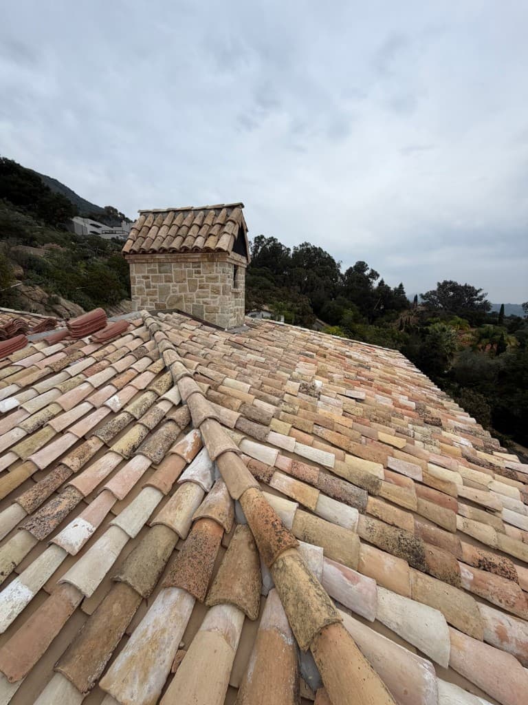 Completed roof with imported Spanish two-piece barrel tiles in weathered terracotta tones and stone chimney