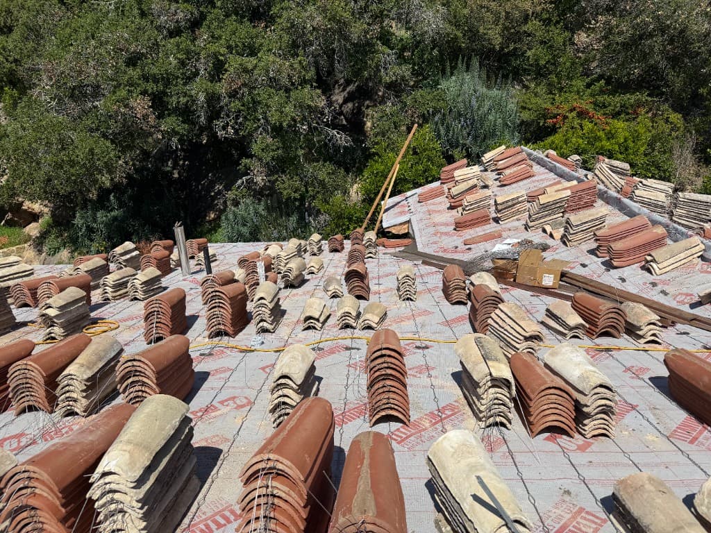 Roof deck prepared with new underlayment and stacks of imported Spanish two-piece clay tiles ready for installation