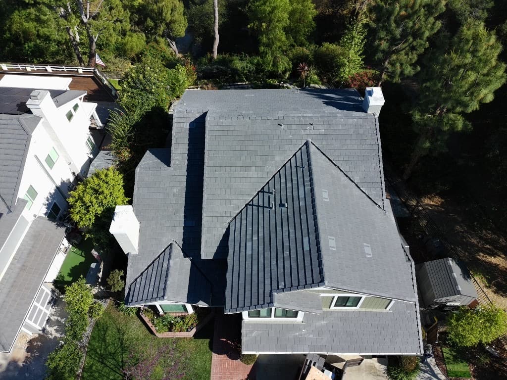 Aerial view of an olive green home with a dark grey tile roof