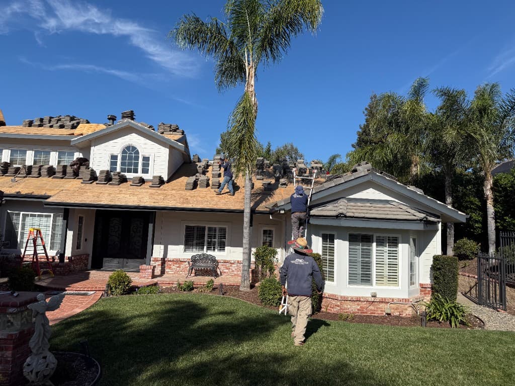 Simi Valley home during tile lift and reset with gray concrete tiles stacked on exposed roof deck and crew on site