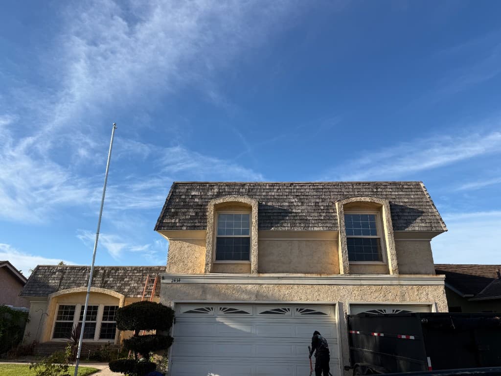 Two-story home with aged wood shake roofing before replacement, with job-site ladder and disposal trailer on site