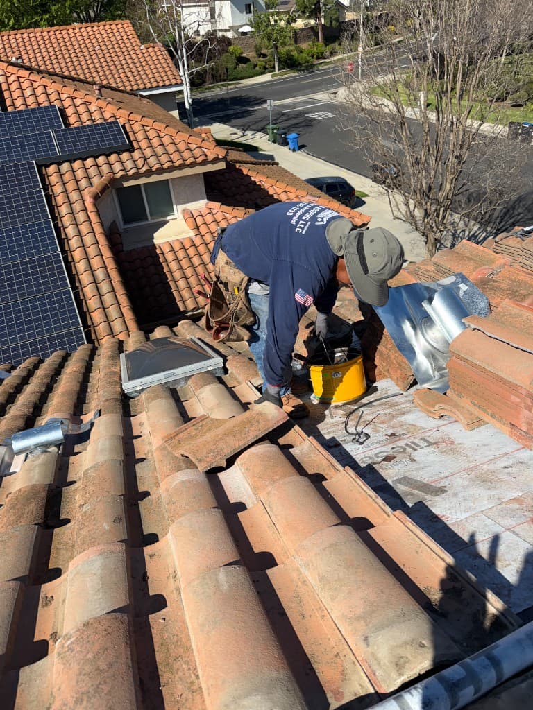 Carrillo Roofing worker repairing terracotta tile roof with TileSeal underlayment near solar panels on a California home